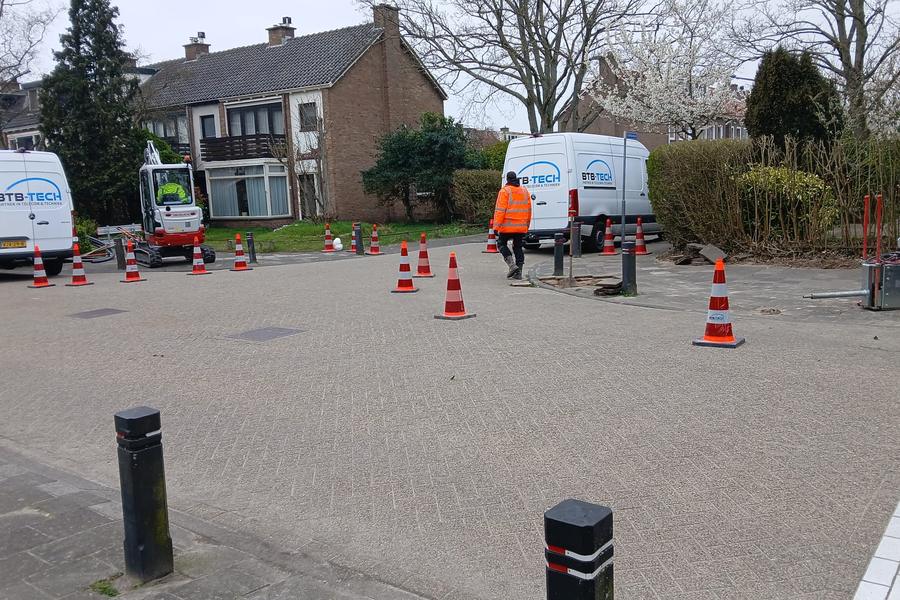 Twee servicebussen en een minigraver bij kabelwerk in een woonwijk