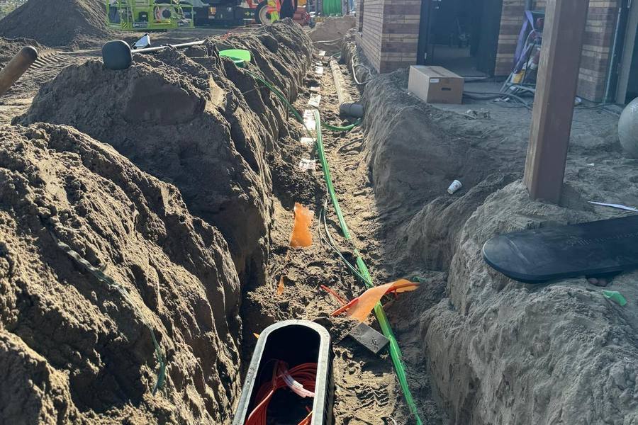 Open sleuf met handhole en microbuizen langs een woning in aanbouw
